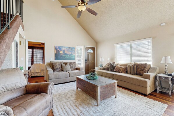 A spacious living room with a high ceiling fan, two sofas, a coffee table, and a lamp.