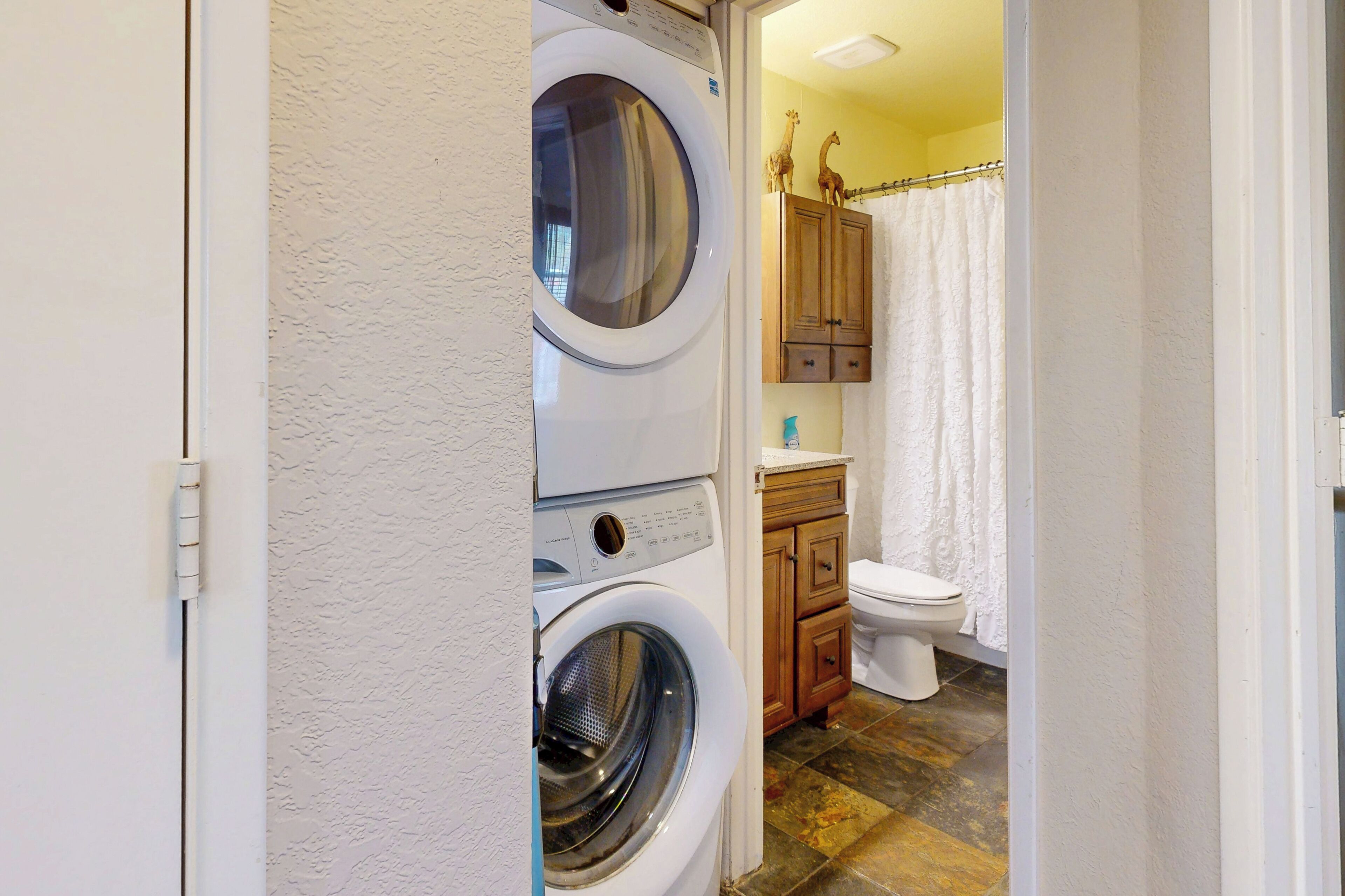 A laundry area with a washing machine and dryer, wooden cabinets, and a toilet in a bathroom.