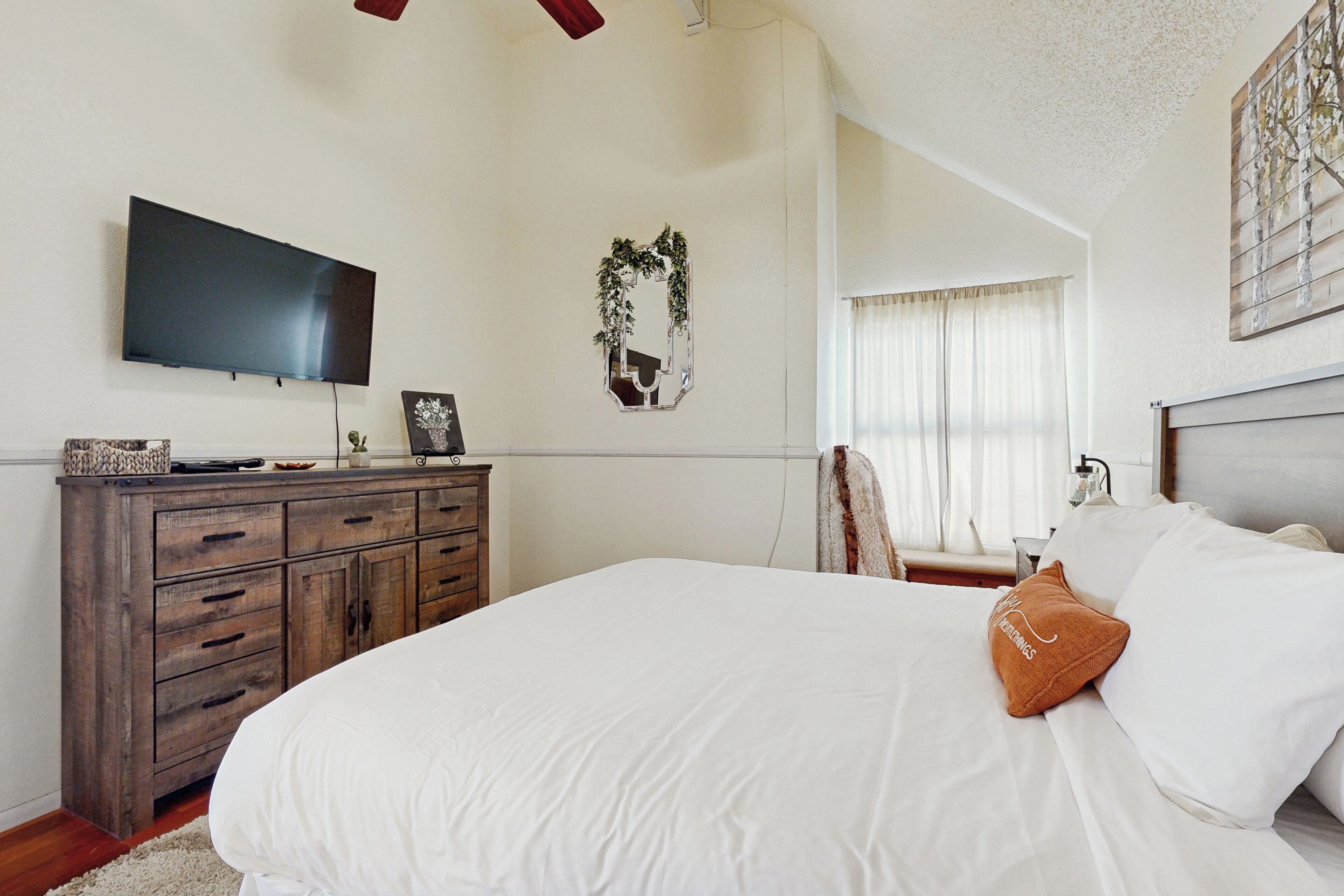 Um quarto com uma cama, penteadeira, televisão e espelho.
