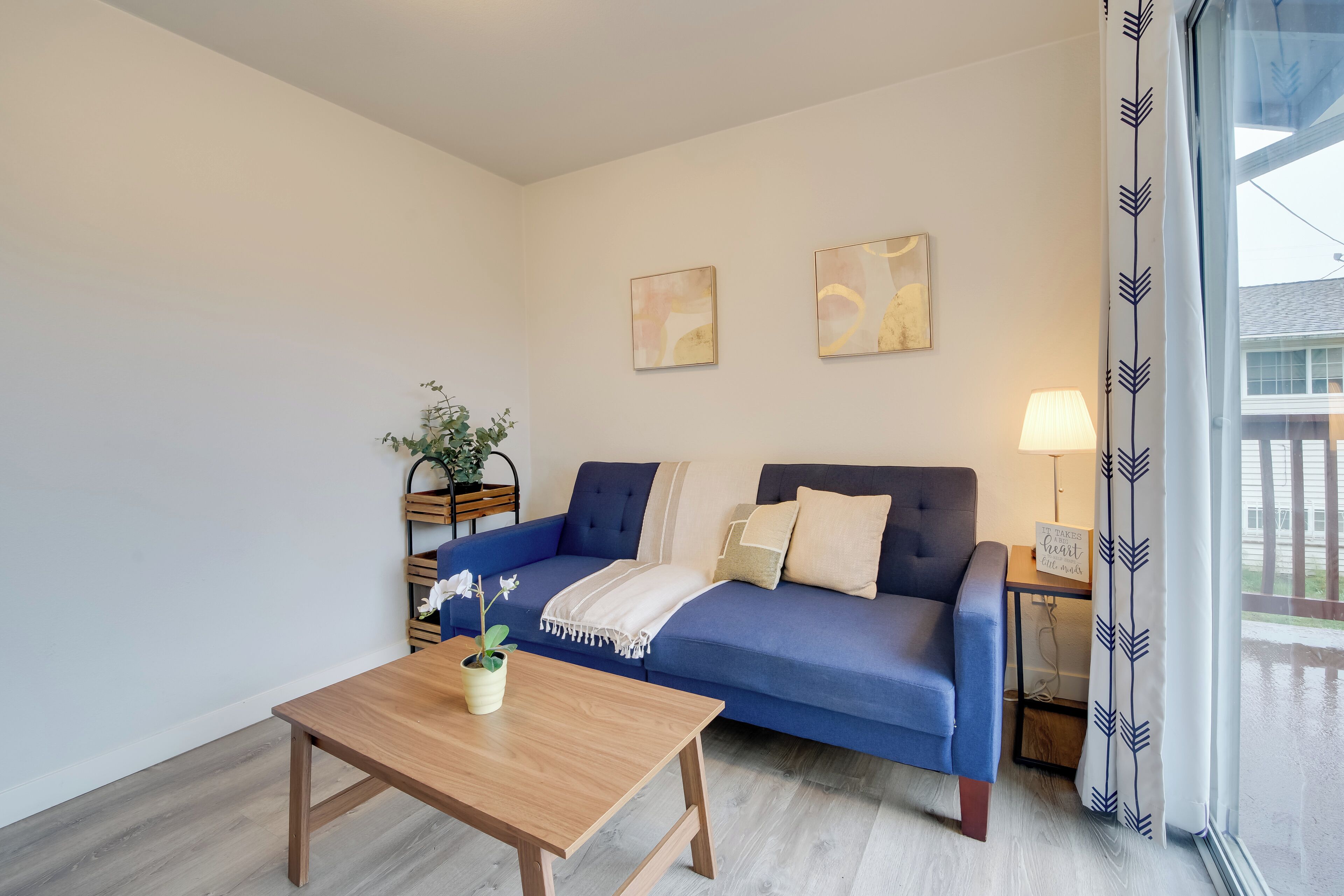 Una sala de estar moderna con un sofá azul, una mesa de centro de madera y dos cuadros colgados en la pared.