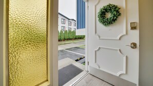 Una puerta blanca con un adorno de laurel verde, una puerta de cristal texturizado y, al fondo, un estacionamiento y edificios.