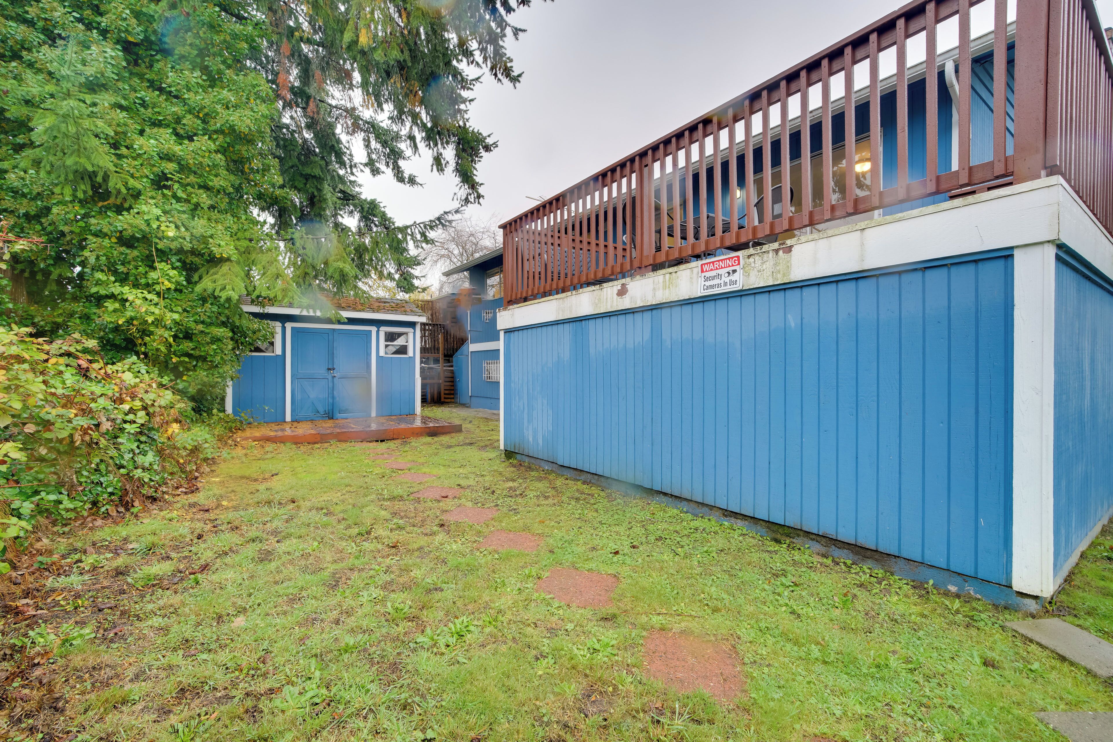 Ein eingezäunter Garten mit einem blauen Gebäude, einer Holzterrasse und einem Warnschild.