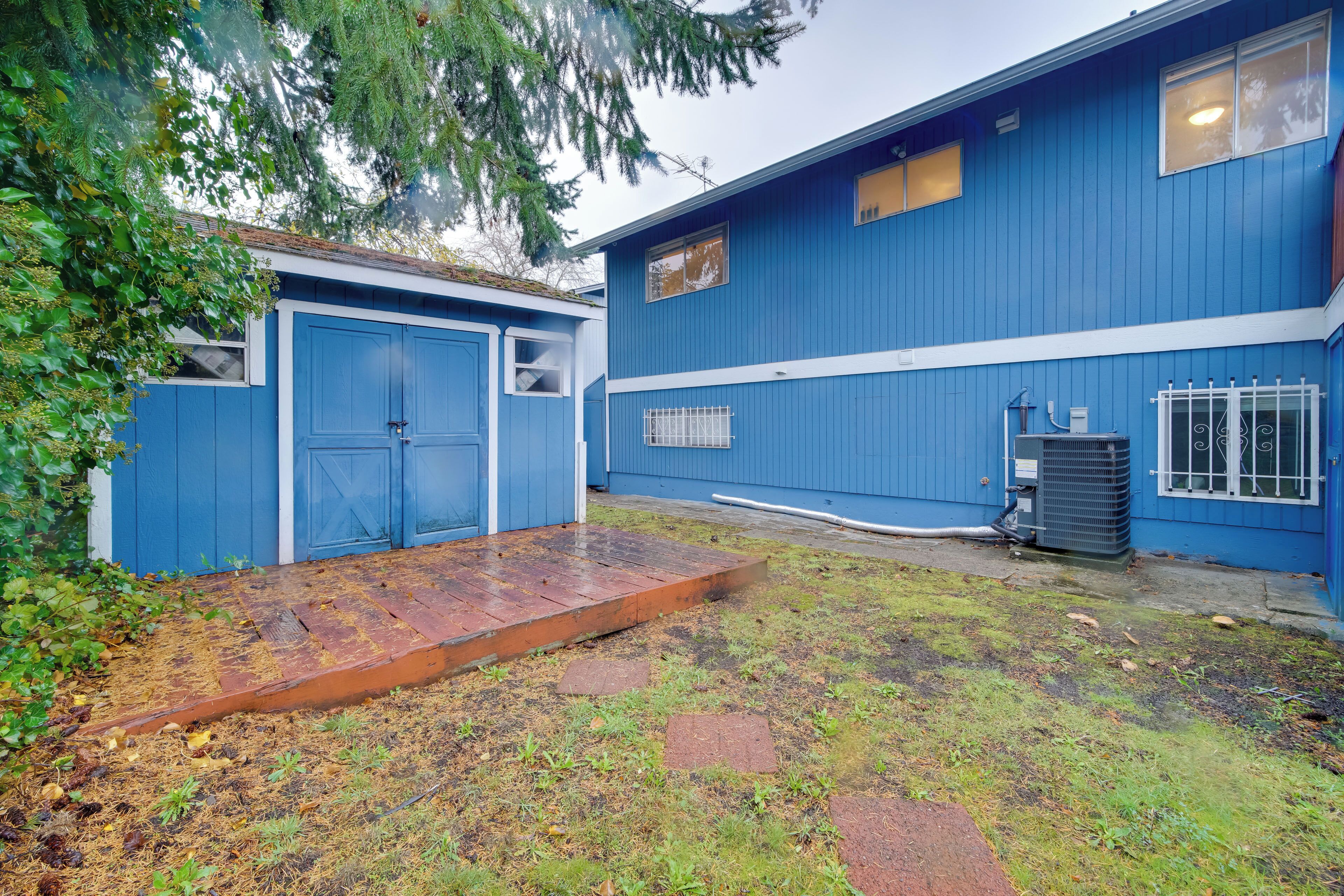 A blue building with a garage, a small outdoor area with a wooden ramp, and an air conditioning unit.