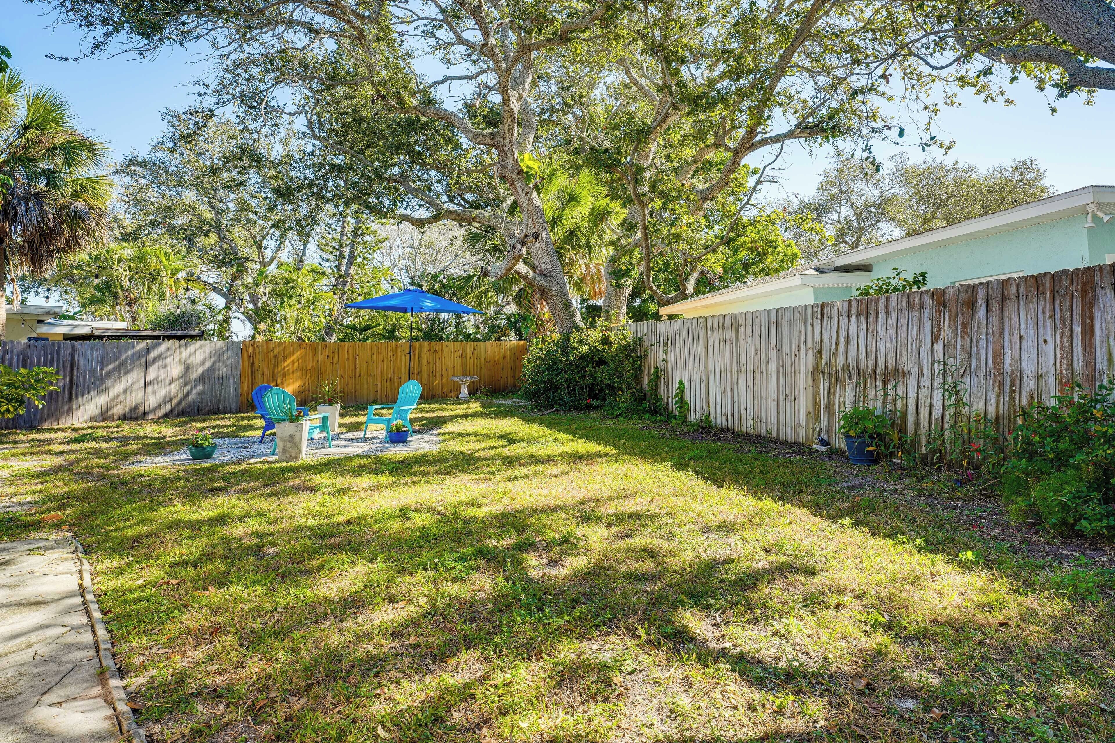 A backyard with a wooden fence, a patio with chairs, and a blue umbrella.