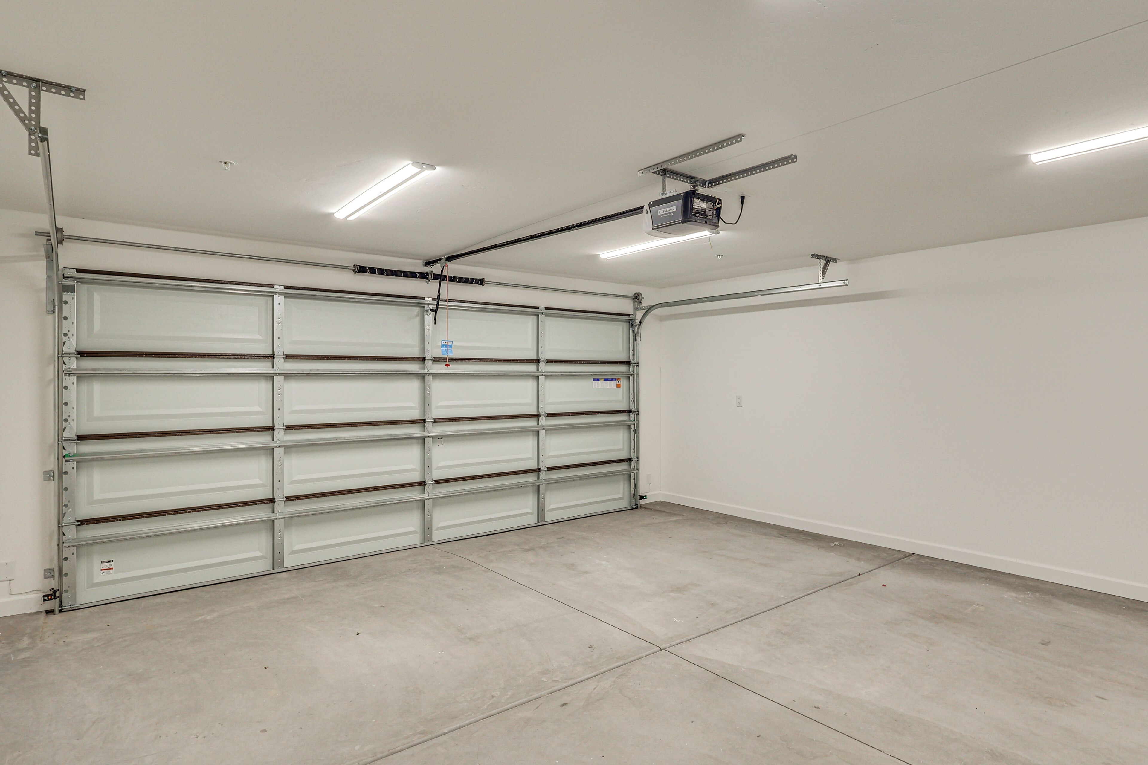 A clean, empty garage with a closed metal garage door, fluorescent lighting, and a ceiling-mounted projector.