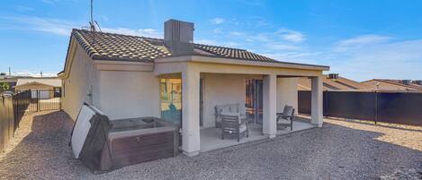 Una casa de un piso con patio, jacuzzi y zona de estar al aire libre techada.