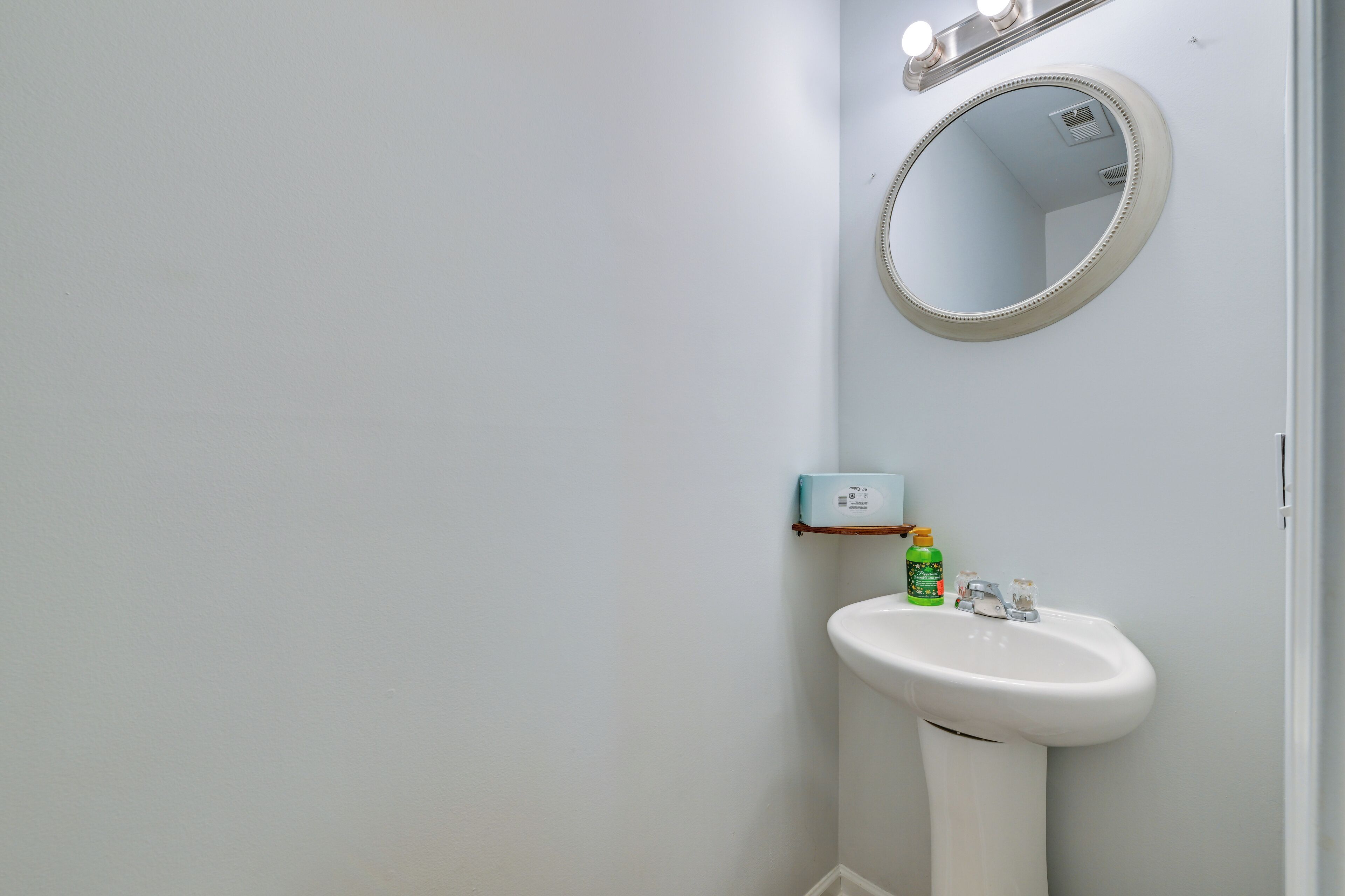 A bathroom with a white sink, a mirror, and a small shelf with toiletries.