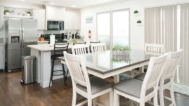 A modern kitchen with white cabinets, stainless steel appliances, and a dining area with a glass table and white chairs. - 3BR Canal-front Home w/ Wifi & Boat Dock (Panama City Beach)