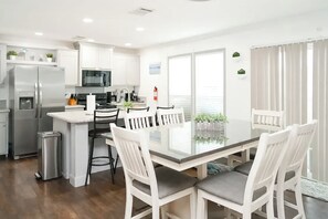 A modern kitchen with white cabinets, stainless steel appliances, and a dining area with a glass table and white chairs. - 3BR Canal-front Home w/ Wifi & Boat Dock (Panama City Beach)