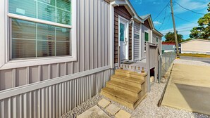 A single-story mobile home with a front porch, a set of steps leading to the entrance, and a small front yard with gravel and stepping stones. - 3BR Canal-front Home w/ Wifi & Boat Dock (Panama City Beach)