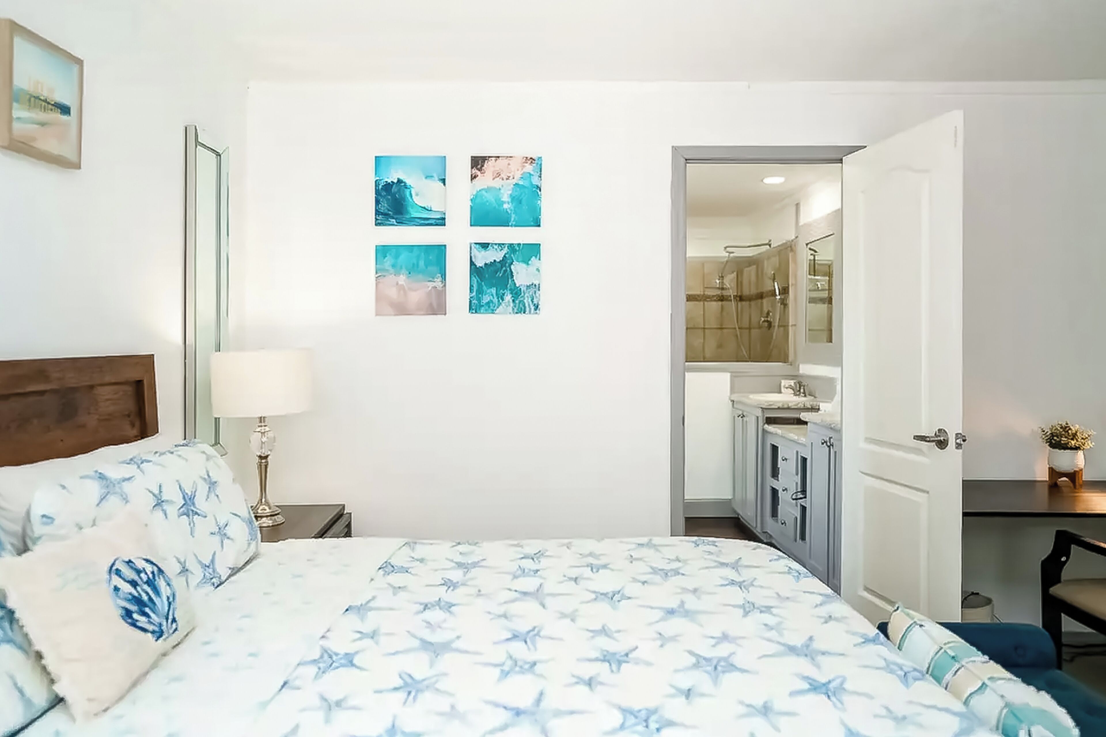Un dormitorio con una cama, una mesita de noche, una lámpara y una pared con cuatro cuadros enmarcados.