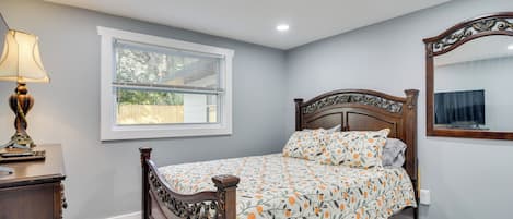 Une chambre à coucher avec un lit en bois, une table de chevet, une lampe, une fenêtre avec des stores et un miroir sur le mur.