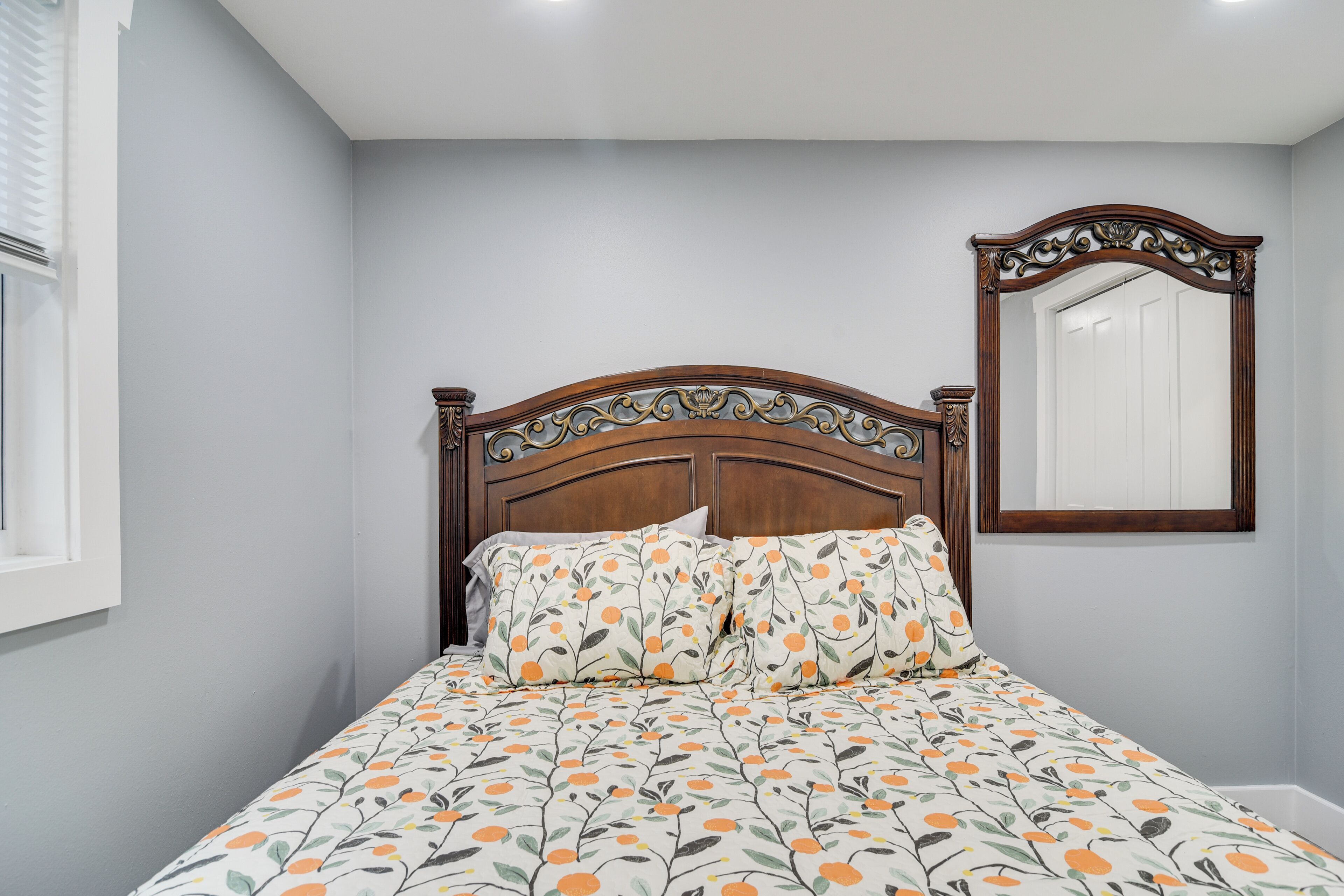 A bedroom with a wooden headboard, a bed with patterned bedding, a bedside table, and a mirror on the wall.