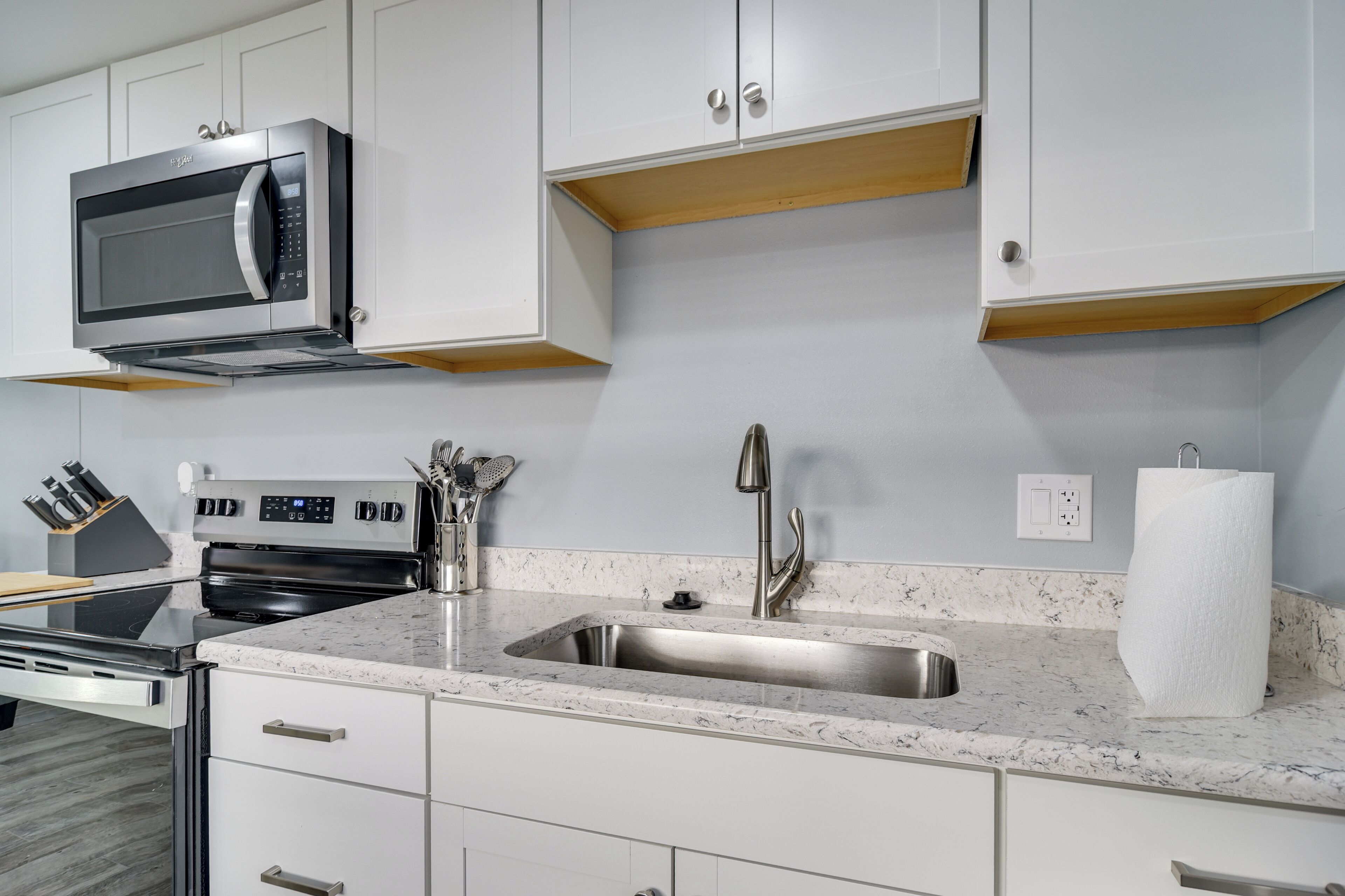 A modern kitchen with white cabinets, a stainless steel microwave, a sink, and a stove.