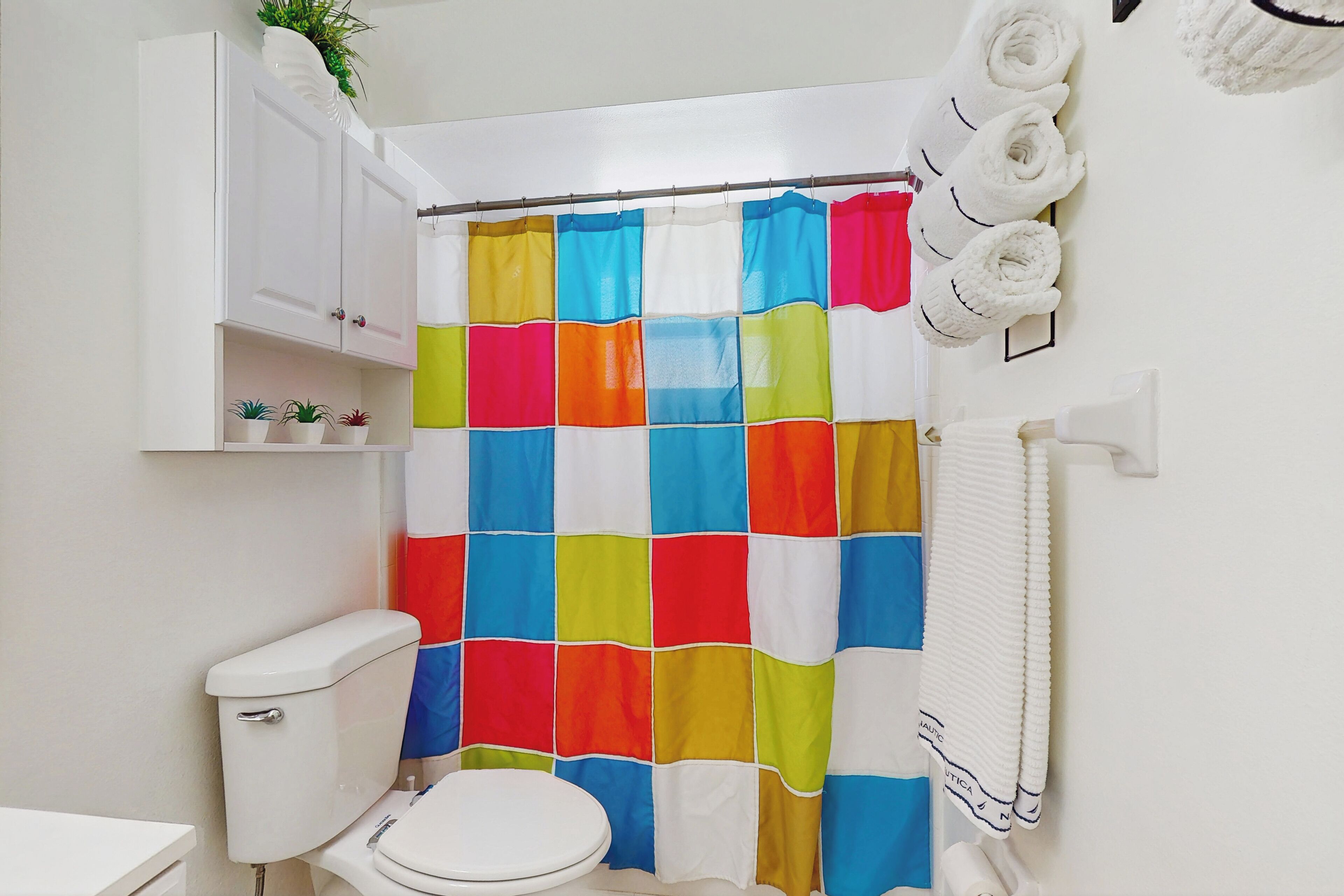 Une salle de bain avec un rideau de douche coloré, des toilettes, un lavabo et un porte-serviettes avec des serviettes.
