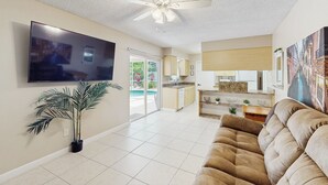 A spacious living room with a large flat-screen TV, a ceiling fan, a potted plant, and a beige sofa. - Pool Access! Dog-friendly Retreat 16 Mi to Orlando (Longwood)