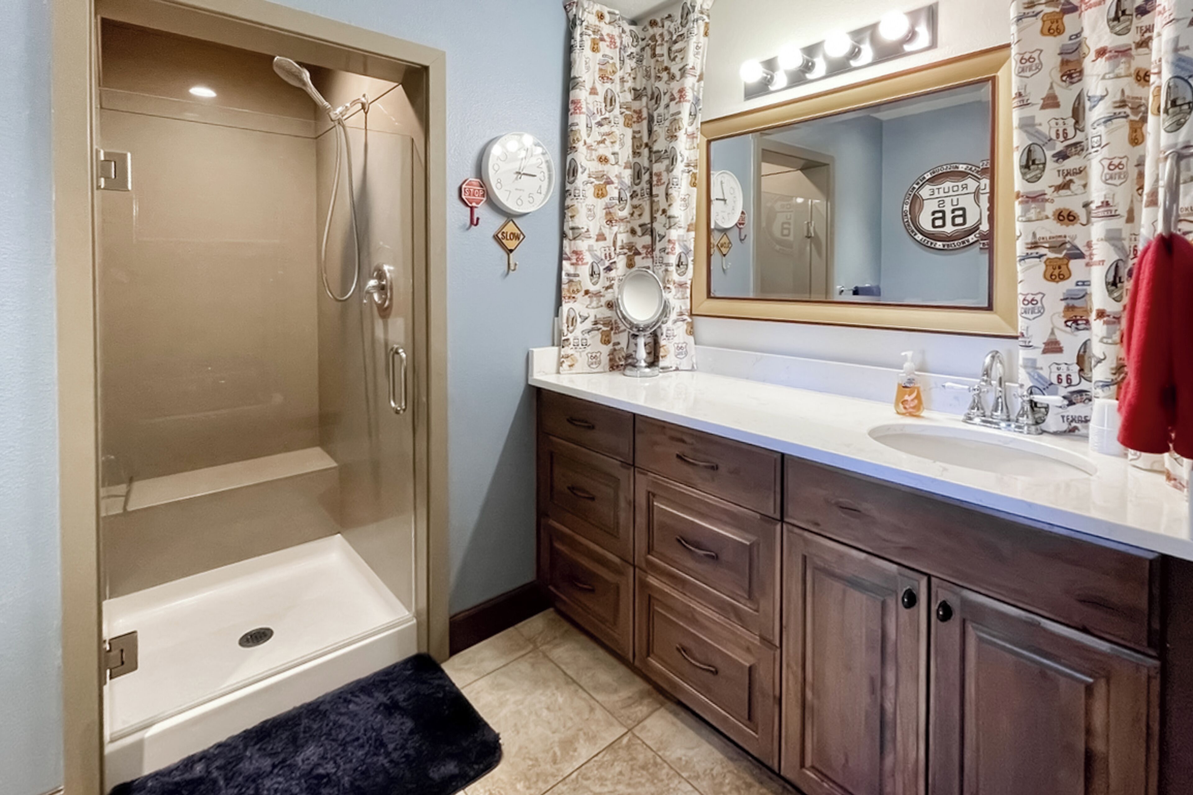 A bathroom with a walk-in shower, a sink with a mirror, and a vanity with drawers.