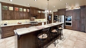 Una cocina moderna con armarios de madera oscura, una isla grande con taburetes de bar, electrodomésticos de acero inoxidable y una lámpara de araña.