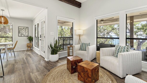 A spacious living room with a large window, a white sofa, a coffee table, and a dining area with a table and chairs. - Lakefront, Private 3br, Dog-friendly Rental (Canyon Lake)