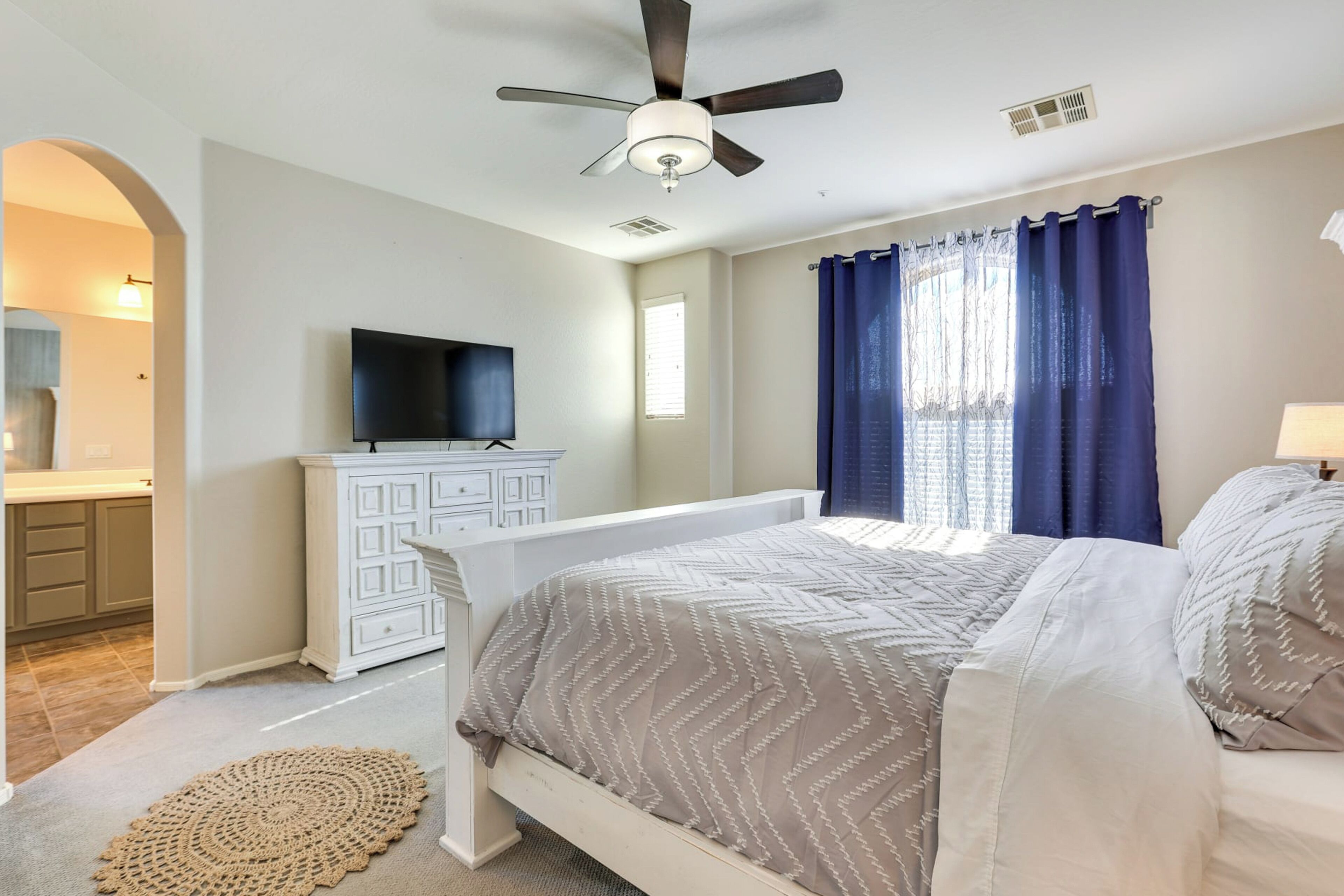 Un dormitorio con cama, ventilador de techo, televisor, cómoda y ventana con cortinas.