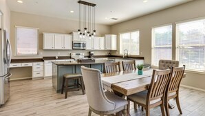 Una cocina moderna con armarios blancos, una isla central y un comedor con sillas y mesa de madera.