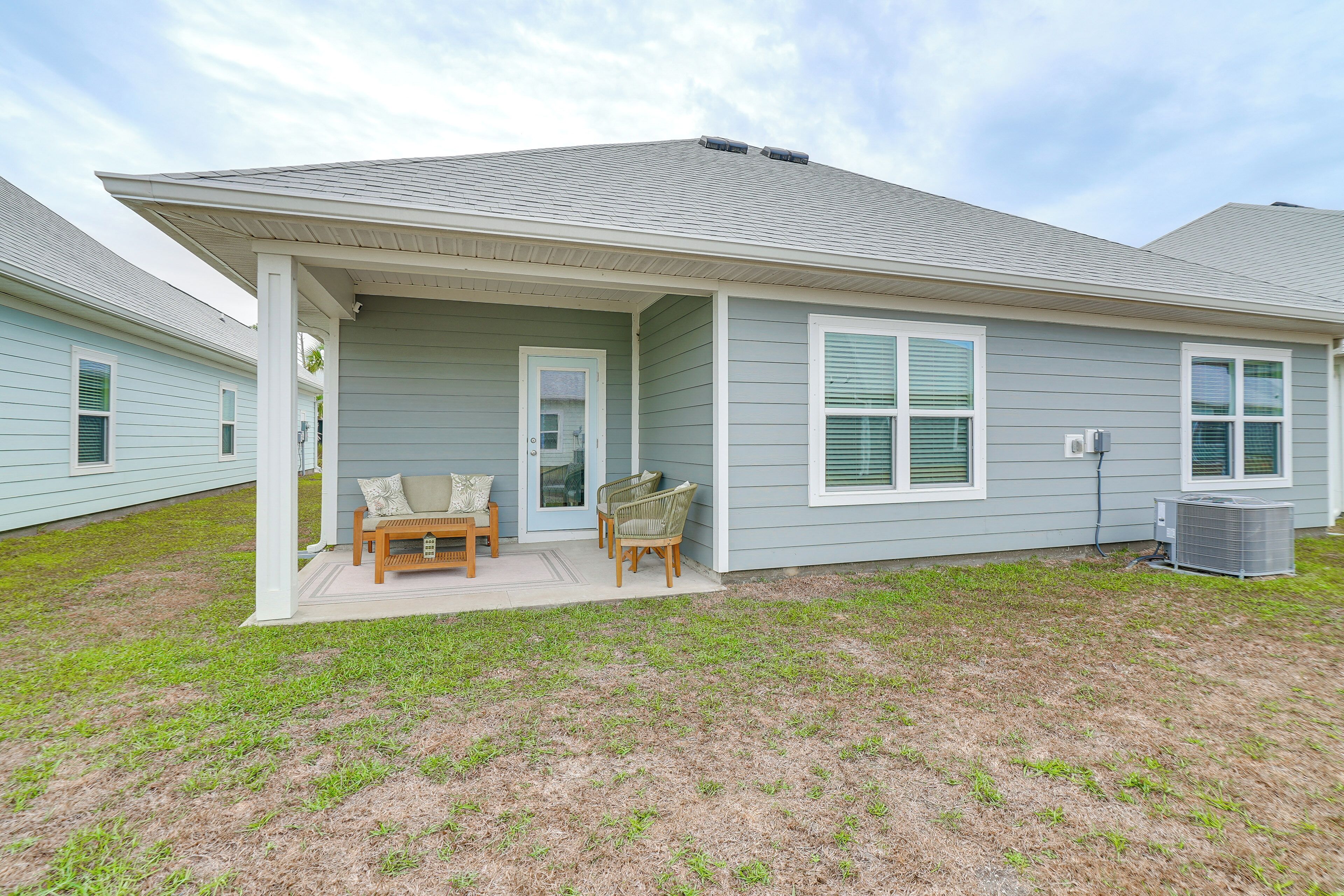 A single-story house with a covered porch, a small patio with a table and chairs, and a lawn.