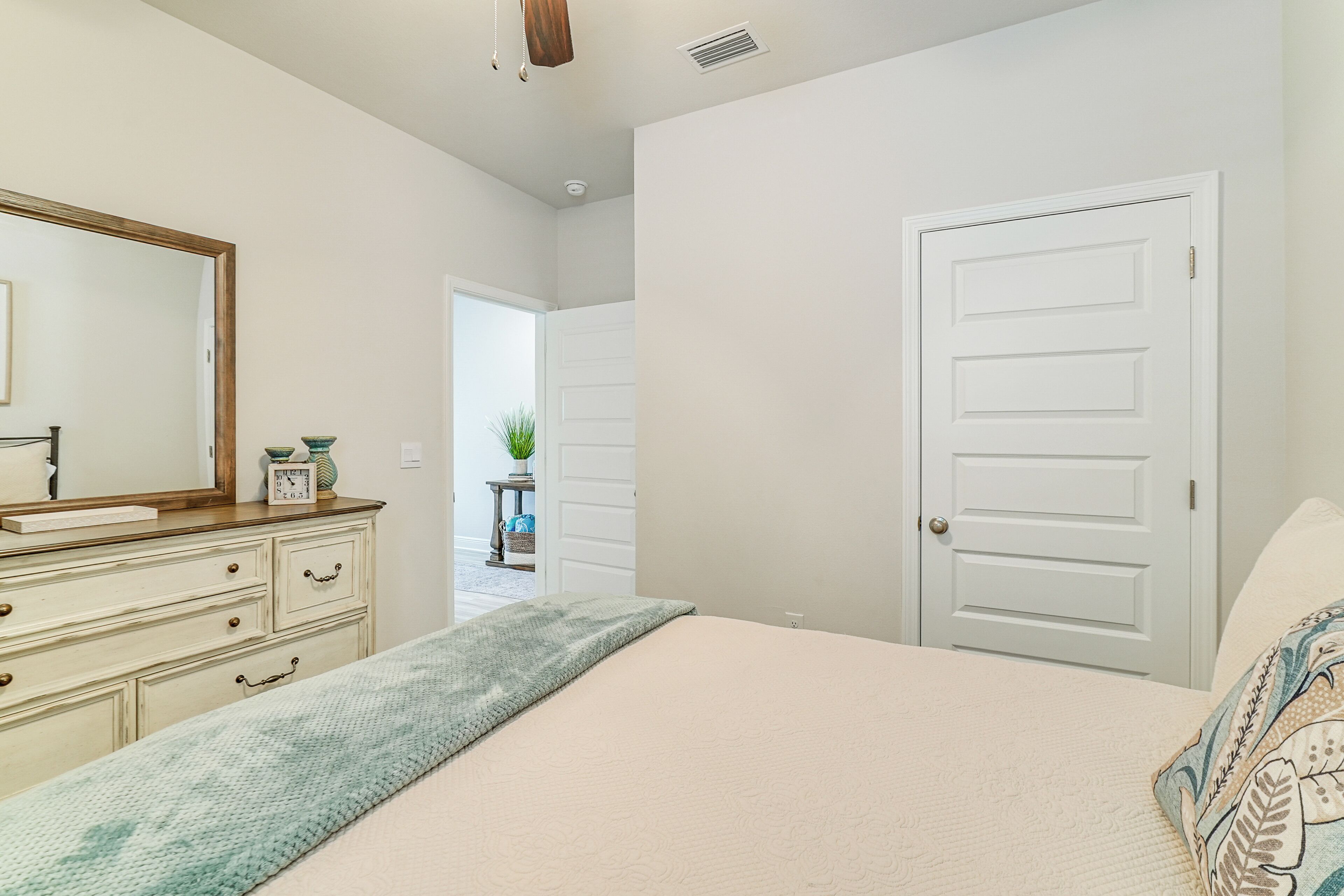 Un dormitorio con cama, cómoda, espejo y una puerta que da a otra habitación.