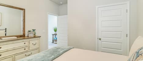 Makuuhuoneessa on sänky, lipasto, peili ja ovi, joka johtaa toiseen huoneeseen.