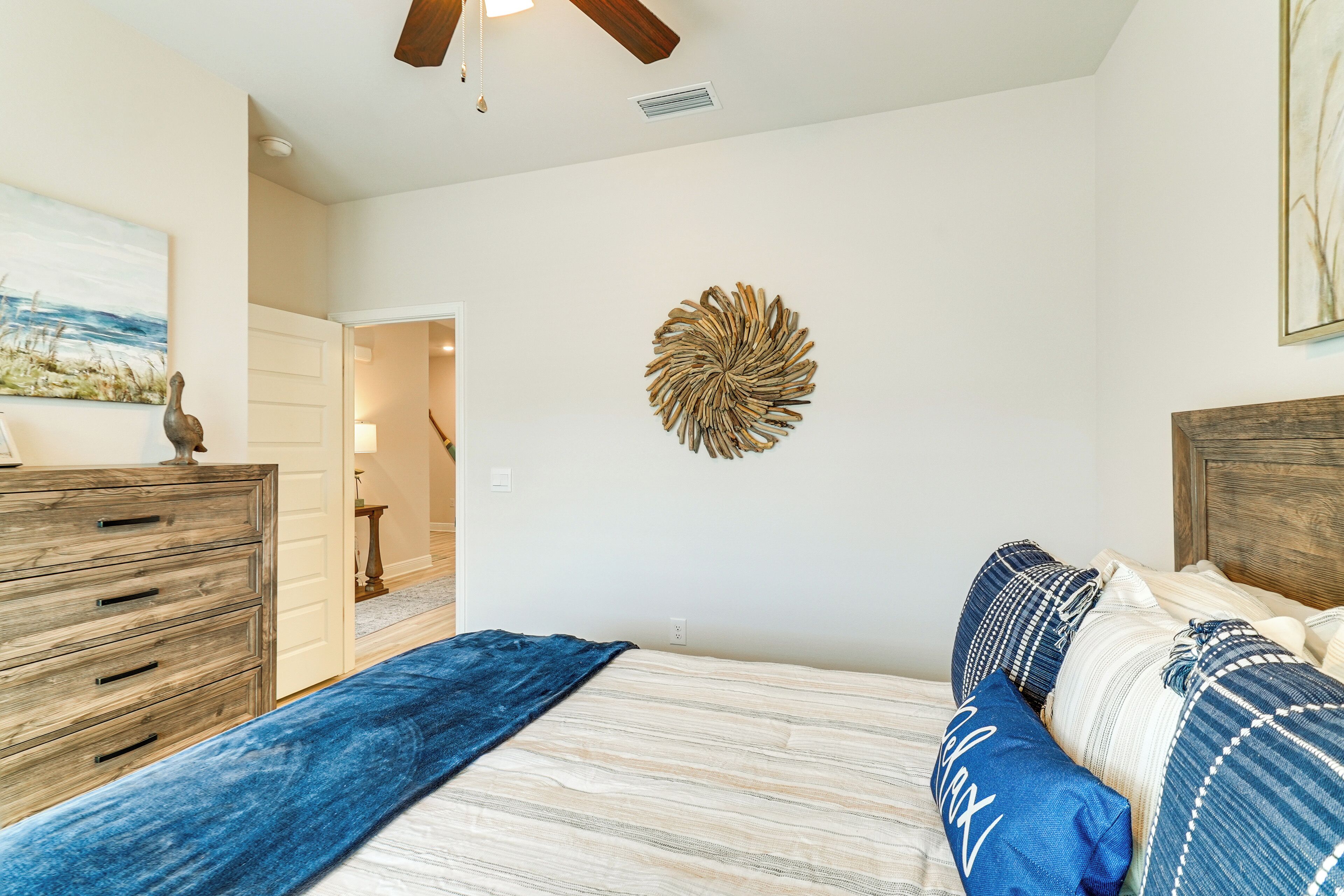 A bedroom with a bed, a dresser, a wall art piece, and a ceiling fan.