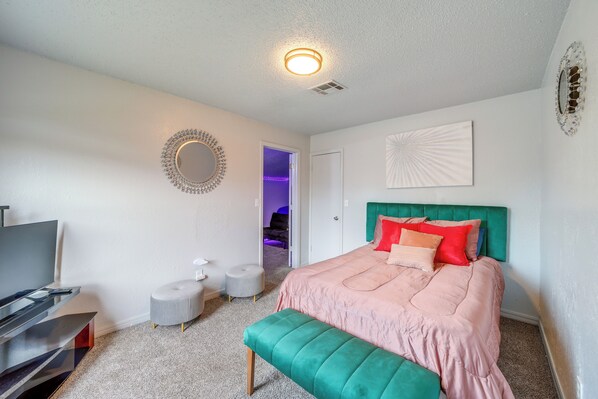 Un dormitorio con cama, televisor, espejo y puerta que da a otra habitación.