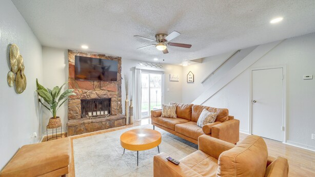 A spacious living room with a stone fireplace, leather sofas, a round coffee table, and a ceiling fan. - 5 Mi to Route 66 Fun! Tulsa Towhome w/ Game Room (Tulsa)