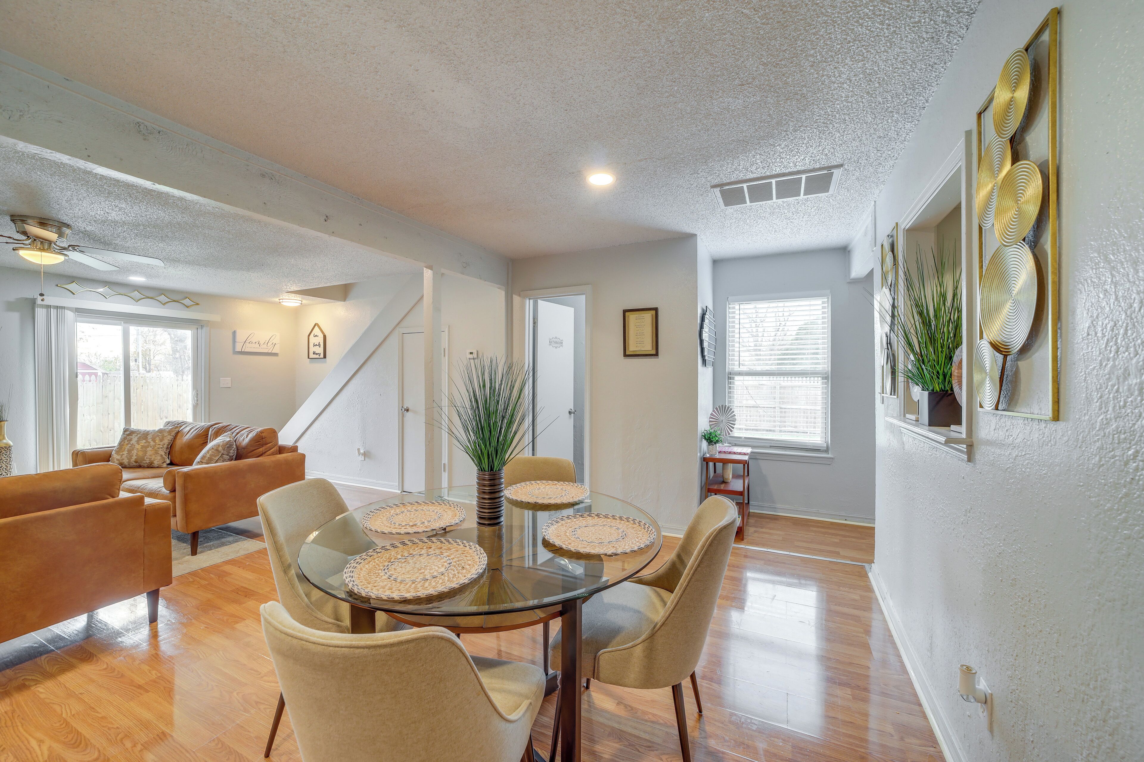 A spacious living room with a glass-top dining table, comfortable seating, and a ceiling fan.