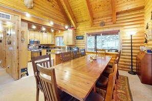 A log cabin interior with a wooden dining table, chairs, a kitchen area with appliances, and a large window. - Quiet 2BR Fireplace Balcony W & D (Brian Head)