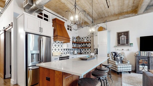 Una cucina moderna con elettrodomestici in acciaio inossidabile, una grande isola con sgabelli da bar e un'area pranzo con una sedia a quadretti e una televisione.