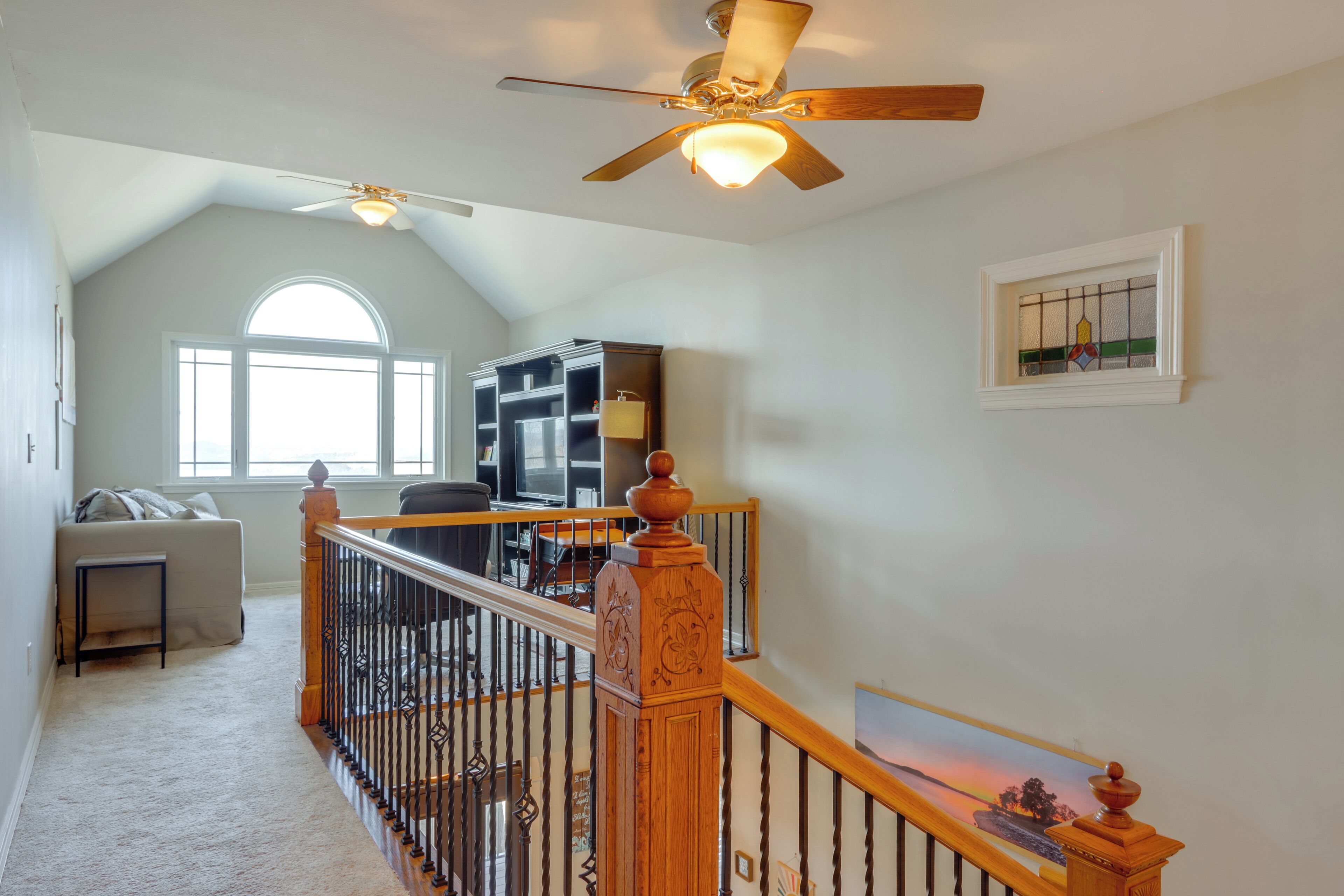 A spacious living area with a high ceiling, a wooden staircase with a railing, a large window, and a ceiling fan.
