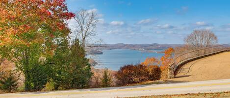 A scenic view of a coastal road with a stone bridge, autumn foliage, and a clear blue sky.