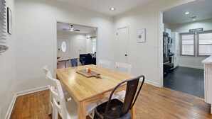 A dining area with a wooden table and white chairs, a kitchen in the background, and a door leading to another room. - Easy Access to Osu! 'marvin's Manor' in Stillwater (Stillwater)
