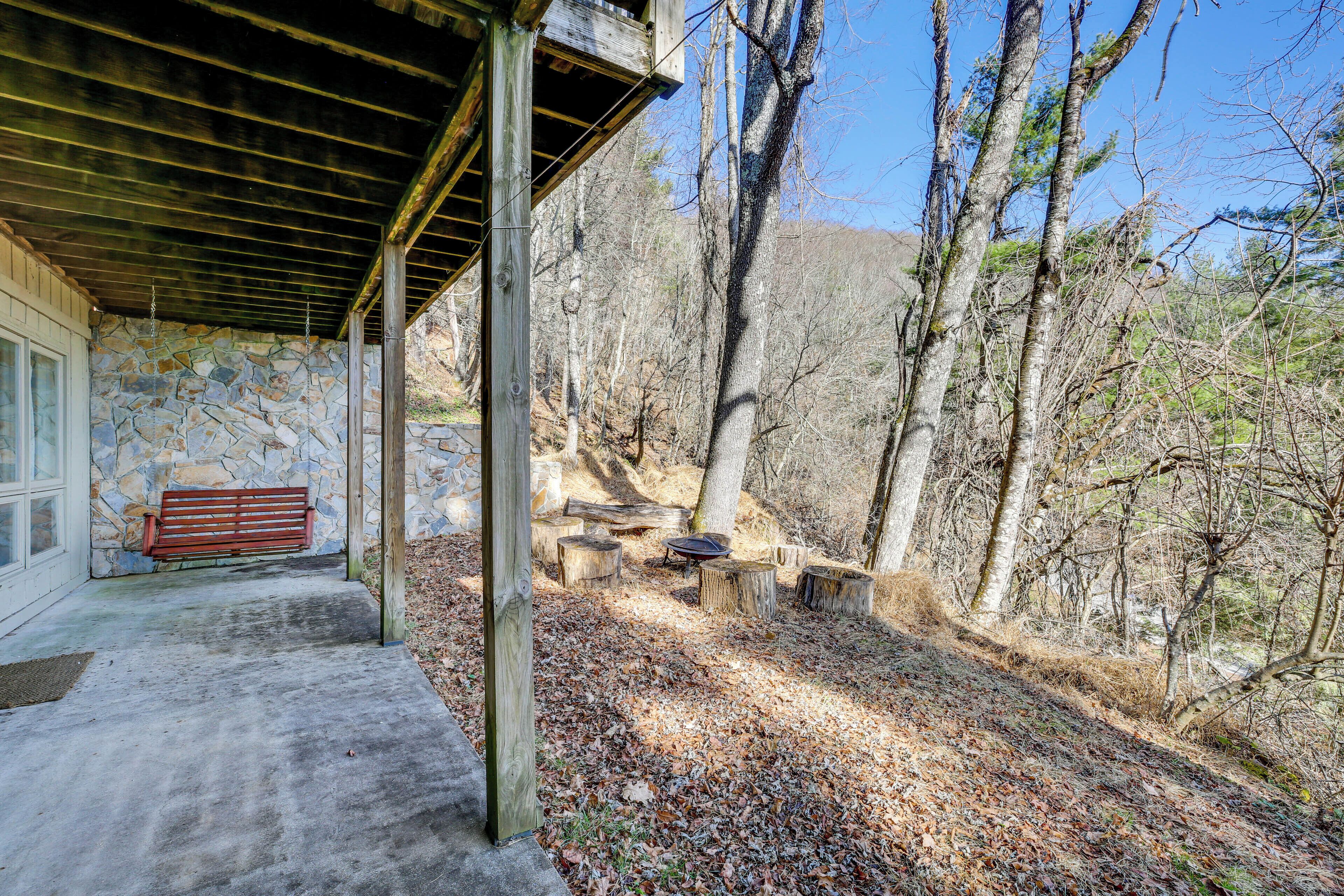 A covered outdoor area with a stone wall, wooden bench, and a fire pit.