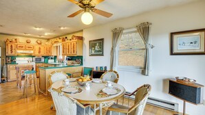 A kitchen with wooden cabinets, a dining table set with plates, and a ceiling fan. - Ski, Hike & Unwind: Mtn-view Gem w/ Deck in Boone (Boone)