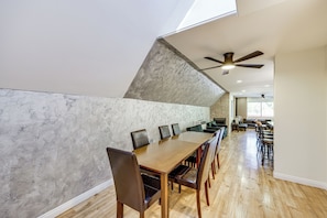 A modern dining area with a long wooden table, multiple chairs, and a ceiling fan.