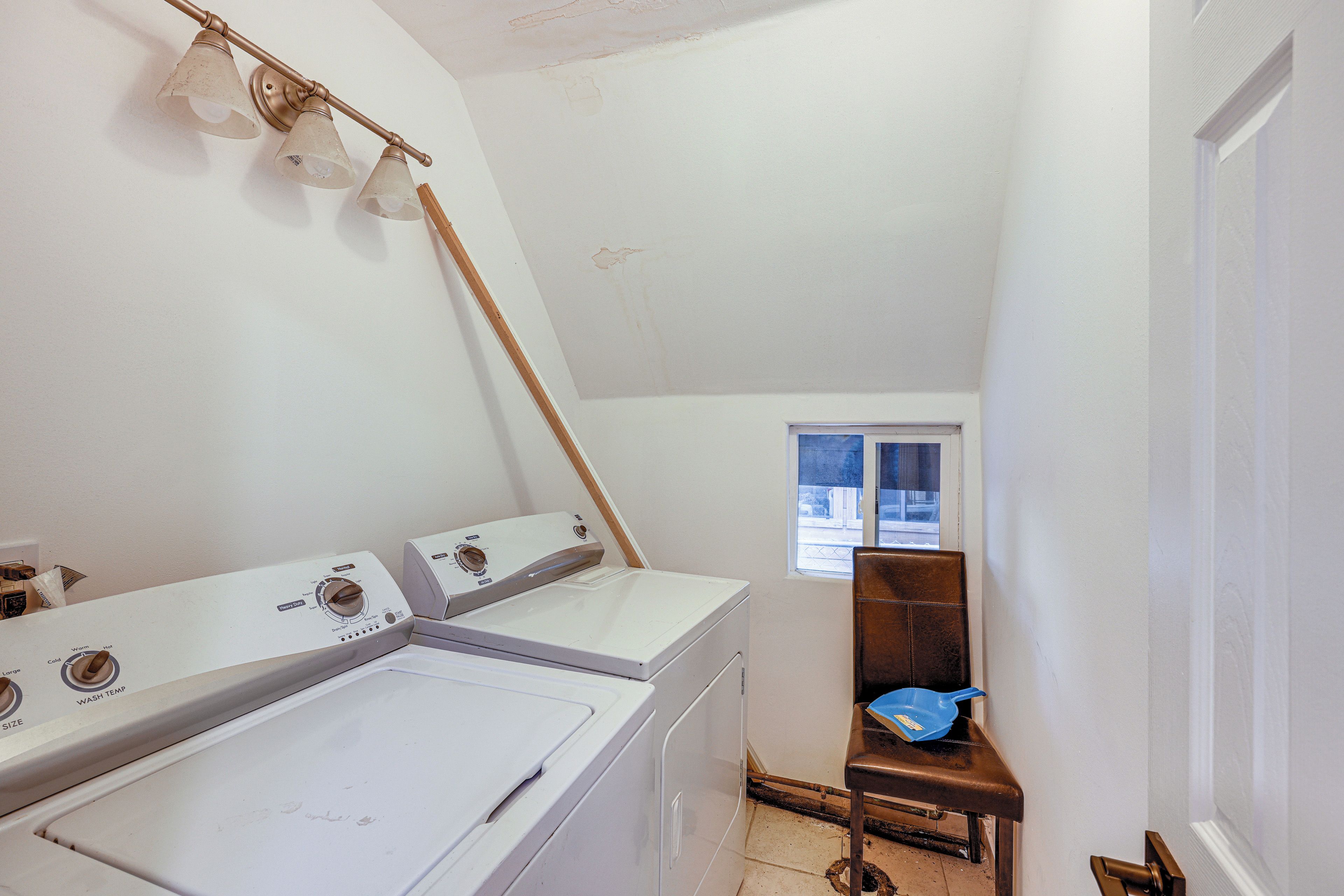 A laundry room with two washers and dryers, a wooden chair, and a window.