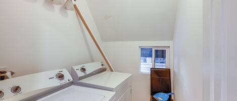 A laundry room with two washers and dryers, a wooden chair, and a window.