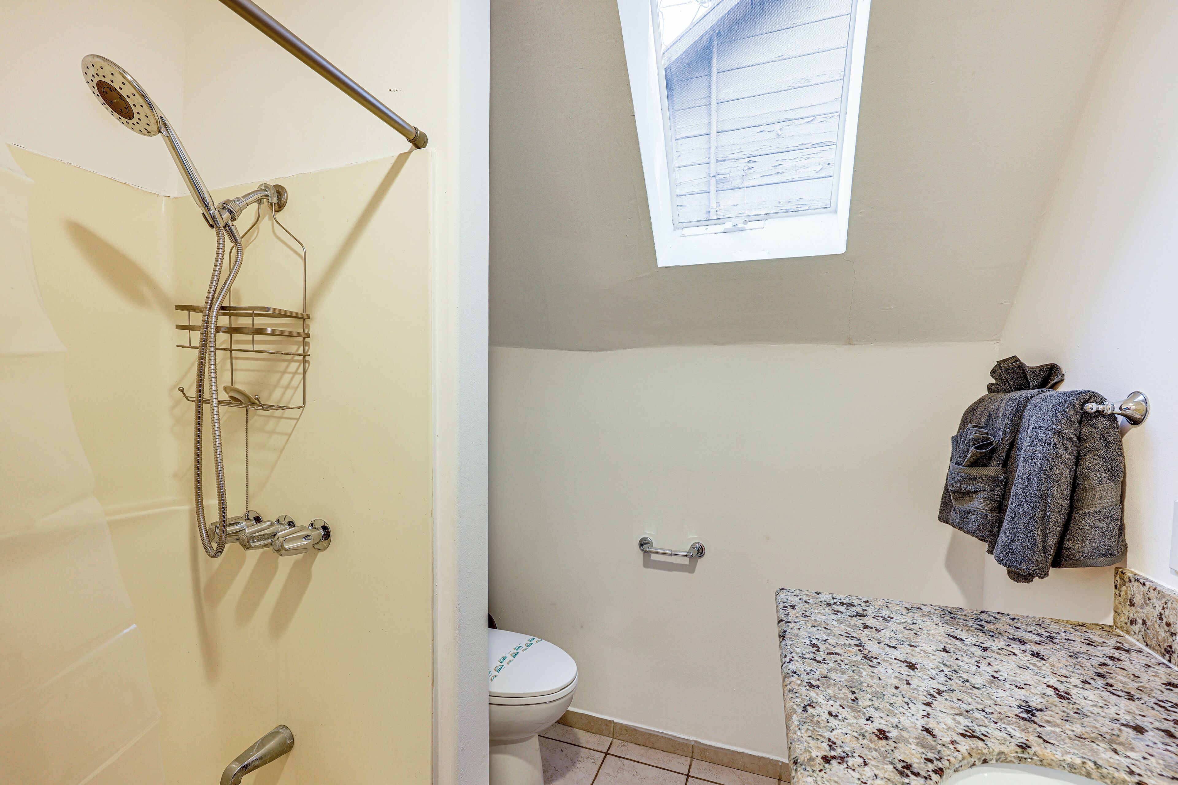A bathroom with a shower, toilet, and a window.