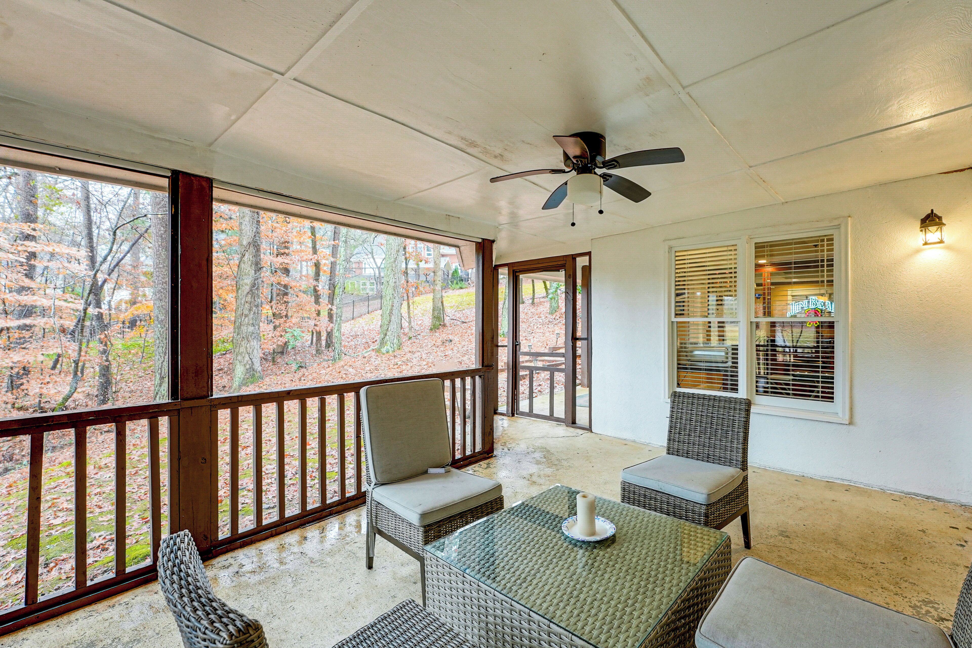 A covered patio with wicker furniture, a ceiling fan, and a view of a wooded area.