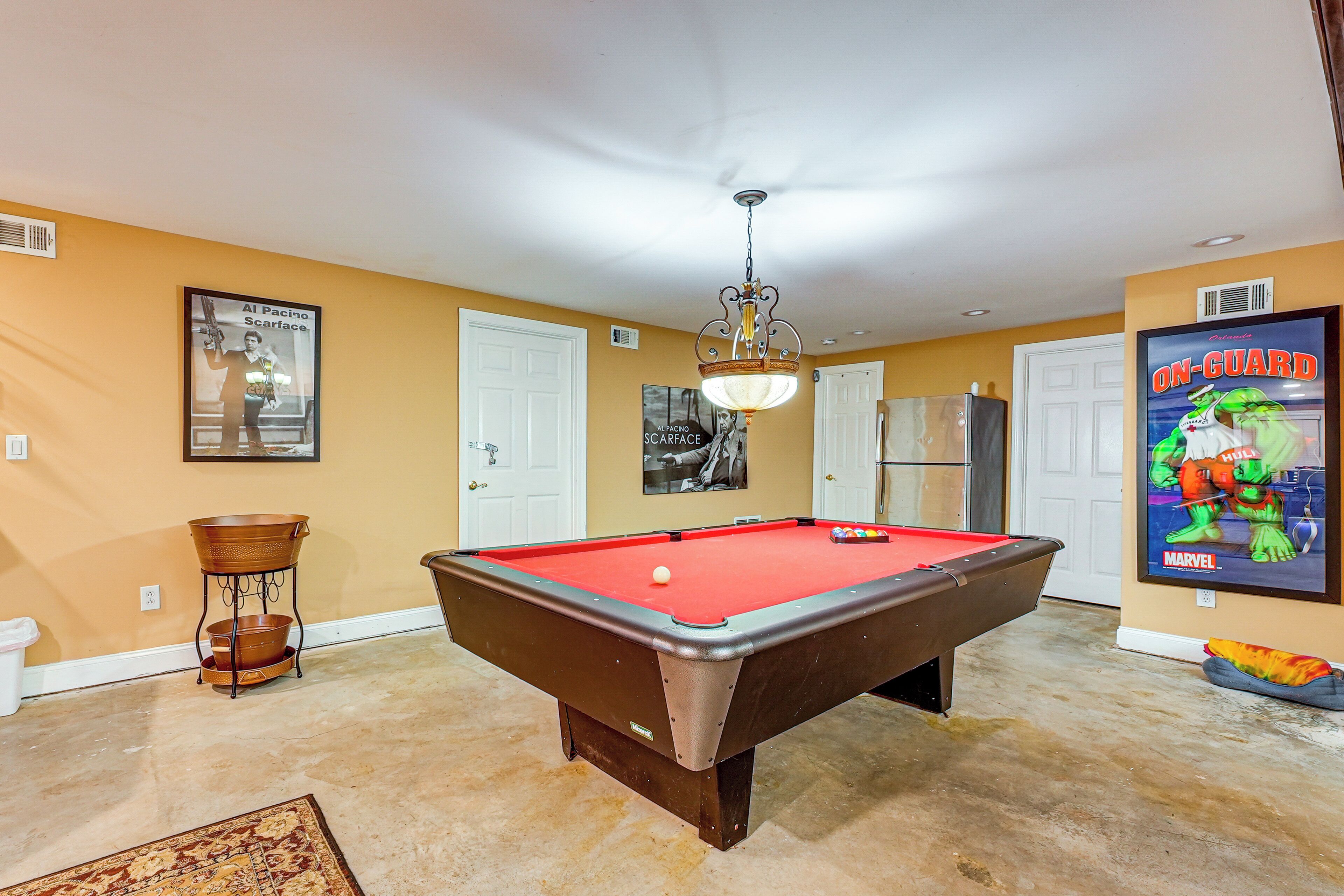 A pool table in a room with yellow walls, a ceiling fan, and a poster of a Marvel character.