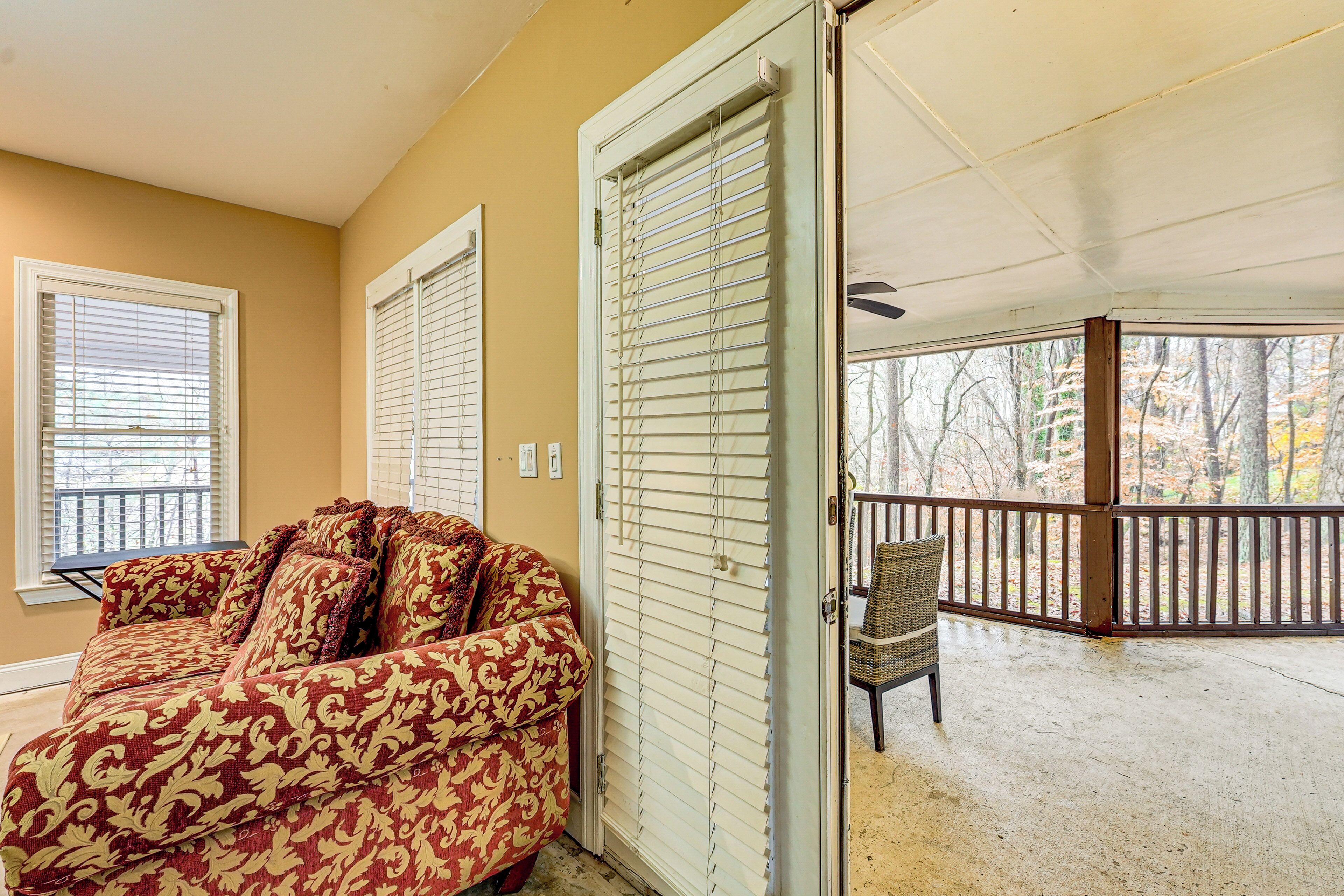 A room with a patterned sofa, a sliding glass door leading to a balcony, and a chair on the balcony.