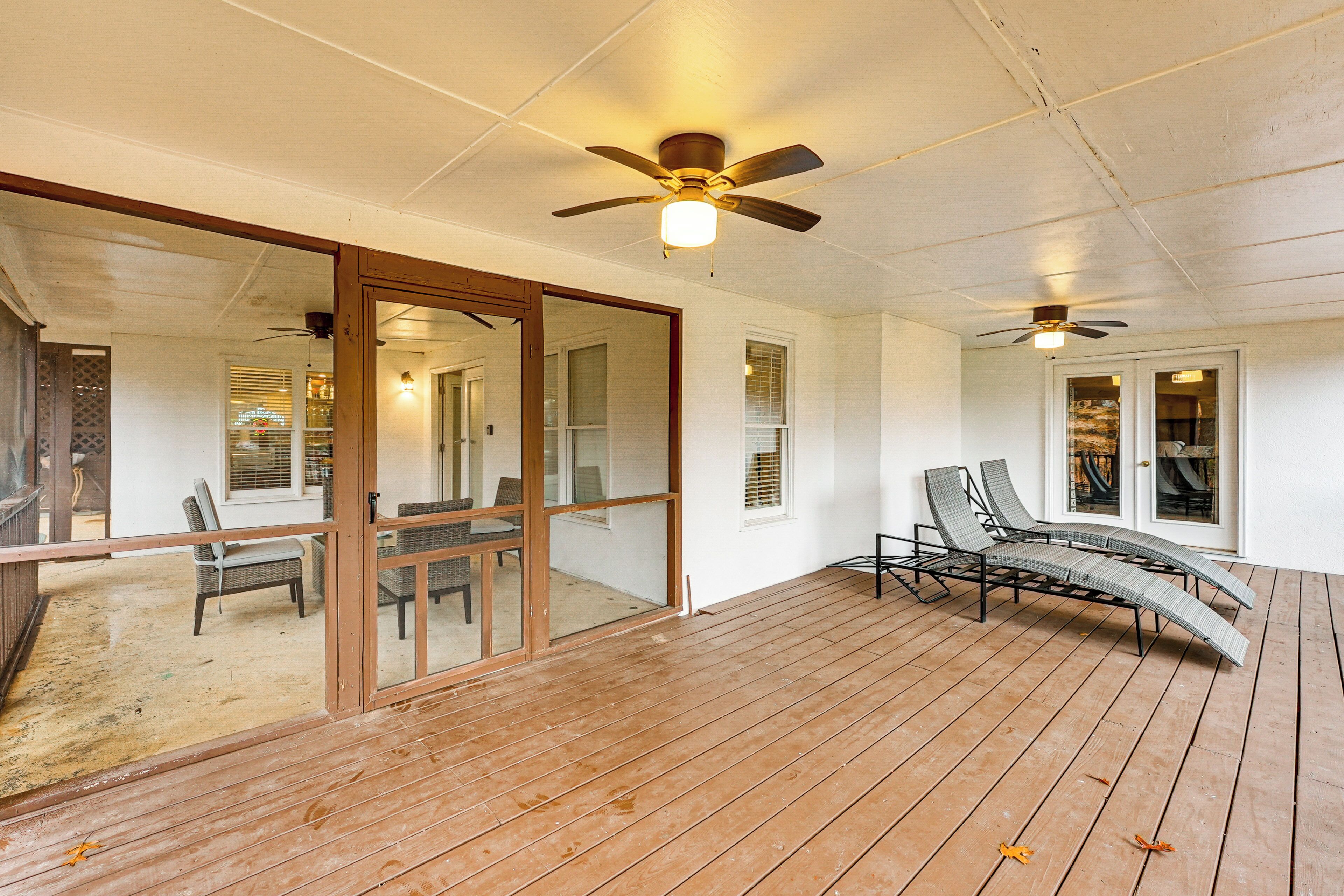A covered wooden deck with ceiling fans, a glass door leading to an interior space, and a lounge chair.