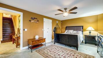 Une chambre à coucher comprenant un lit, un ventilateur de plafond, une table de chevet, une commode, un tapis et un escalier menant à une autre pièce.