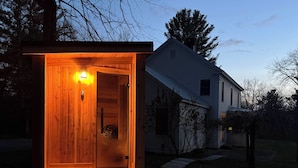 A wooden cabin with a lit interior, a door, and a small porch area. - Close to Copake Lake! 4-season Escape w/ Sauna (Copake)
