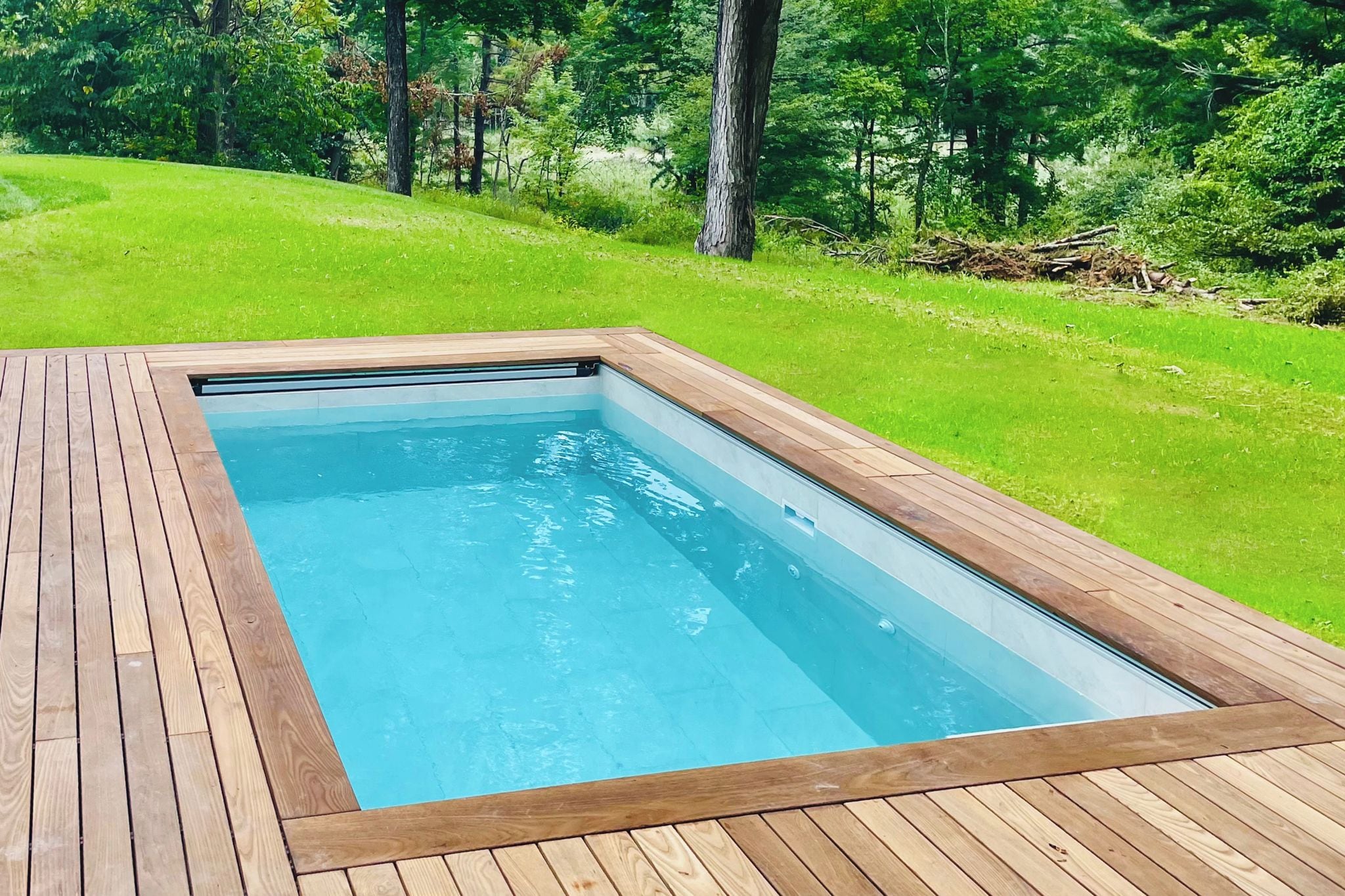 A rectangular swimming pool with a wooden deck surrounding it.